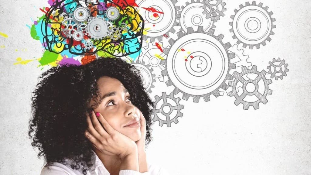 A woman rests her chin in her hands beneath an illustration of a colorful brain and sketched gears