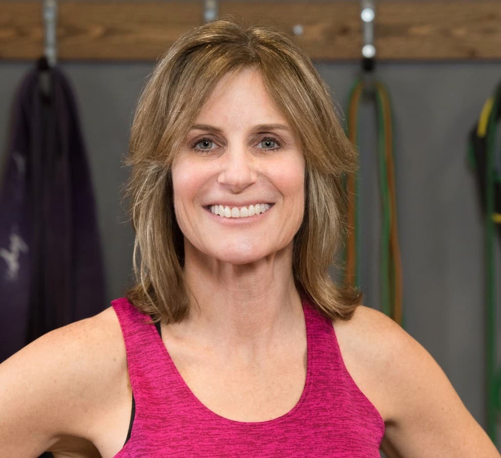 A smiling woman in a pink tank top stands in a gym.