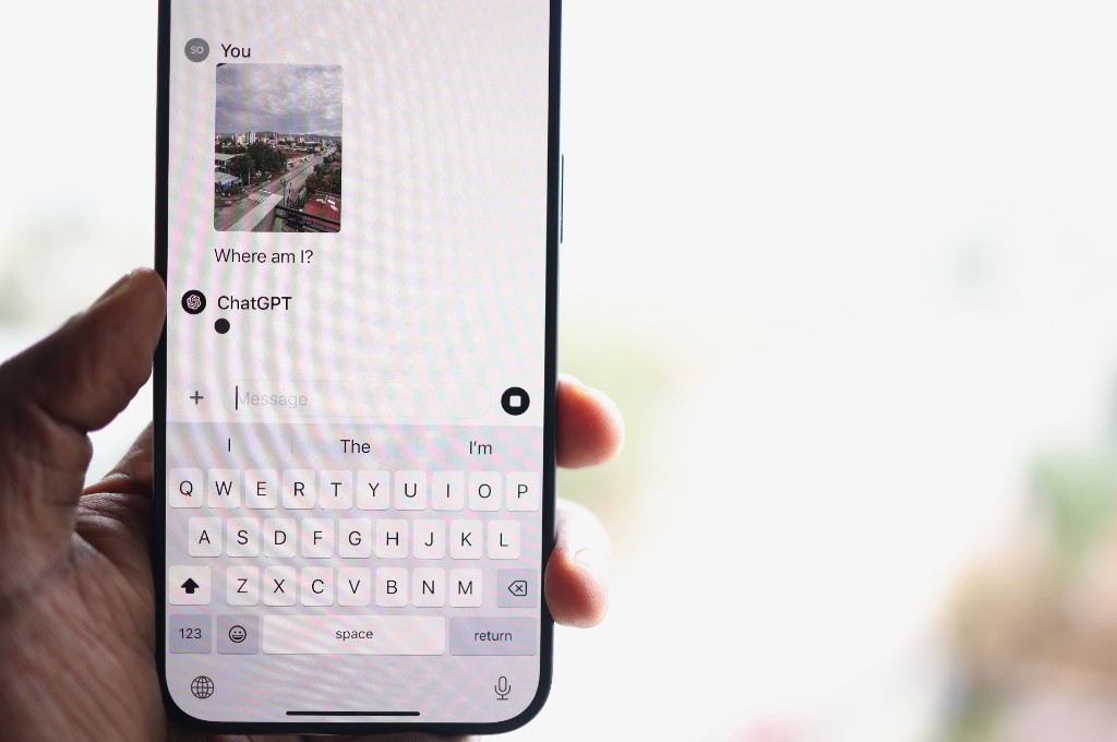 A person holds a phone showing a ChatGPT conversation with the question "Where am I?"